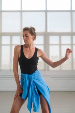 Bir kadın, geniş pencereli parlak bir stüdyoda çağdaş bir dans sergiliyor. Duruşu hareketi ve esnekliği vurguluyor, fitness, dans ve yaşam tarzı tasvirleri için ideal hale getiriyor..