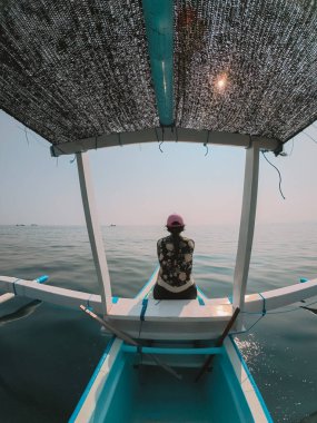 Balıkçı teknesinin pruvasında oturan uzun kollu mayo giymiş genç bir kadın. Dalış ve şnorkelle yüzme turu. Tropikal ülke ve deniz maceralarında tatil.