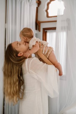 Küçük kızını kucağında tutan ve onunla oynayan genç bir kadın. Sevimli bebek mutlu bir şekilde gülümsüyor. Bebeği uyutmak için sallıyorum. Anneler Günü. Aşk ve sevgi.