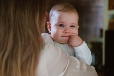 Annesi tarafından tutulan sevimli bir bebek kızın yakın plan portresi. Kocaman mavi gözleri ve tatlı bir gülümsemesi var. Yeni doğmuş bir bebeğin sağlığı ve bakımı. Emzirme. Doğum izni mi? Anneler Günü.
