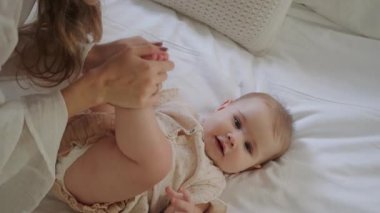 Küçük bir kız bebek beyaz bir battaniyenin üzerinde yatar, anne kızın üzerine eğilir, bacaklarını eline alır ve onlarla oynar, bir şarkı söyler. Doğum izni mi? Anneler Günü.