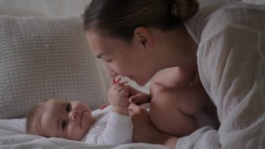 Büyüleyici bir bebek, annesinin yanındaki beyaz bir battaniyenin üzerinde uzanmış, ona gülümseyen, onunla konuşan ve onu şefkatle öpen genç bir kadındır. Anne ve kızı. Sevgi ve ilgi. Anneler Günü