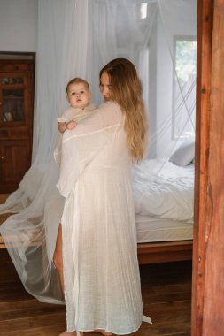 Küçük kızını yatak odasında kollarında tutan genç bir kadının portresi, şefkatle ona bakıyor, başını okşuyor. Emzirme. Doğum izni mi? Anneler Günü.