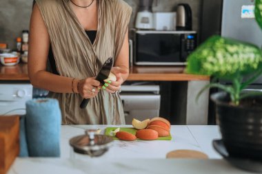Genç bir kadının mutfakta durup masada taze kırmızı elma keserken ellerini yakın çekim yapın. Bir bıçak tutuyor ve sağlıklı bir aperatif hazırlayan bir elma soyuyor. Vejetaryen ürünü. Diyet ve sağlıklı yemek..