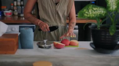 Genç bir kadının mutfakta durup masada taze kırmızı elma keserken ellerini yakın çekim yapın. Bir bıçak tutuyor ve sağlıklı bir aperatif hazırlayan bir elma soyuyor. Vejetaryen ürünü. Diyet ve sağlıklı yemek..