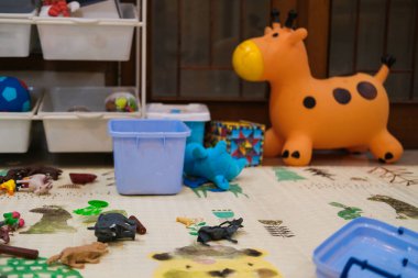 Oyuncakların etrafa saçıldığı bir çocuk oyun odası manzarası. Yerde yumuşak bir halı ve kutular var. Hayvan figürleri ve diğer eğitici oyuncaklar var. Bebekler için anaokulu. Kimse yok..