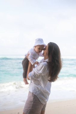 Bebeğini kumsalda döndüren ve onunla oynayan bir annenin portresi. Aile deniz tatili. Anneler oğlunu sever. Anneler Günü.