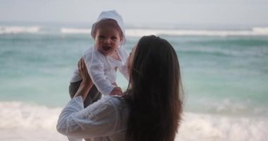 Bebeğini kumsalda döndüren ve onunla oynayan bir annenin portresi. Aile deniz tatili. Anneler oğlunu sever. Anneler Günü.