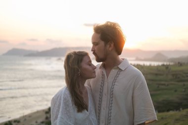 Genç bir kadın ve erkek doğada gün batımına karşı öpüşüyorlar. Balayı, düğünden sonra aşık bir çift. Okyanusun kenarında romantik bir randevu. Sevgililer Günü. Aşk ve romantik ilişkiler.