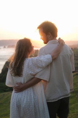 Genç kadın ve erkek doğada gün batımına karşı sarılıyorlar. Balayı gezisi, düğünden sonra aşık bir çift. Tepedeki okyanusta romantik bir randevu. Sevgililer Günü. Aşk ve romantik ilişkiler.