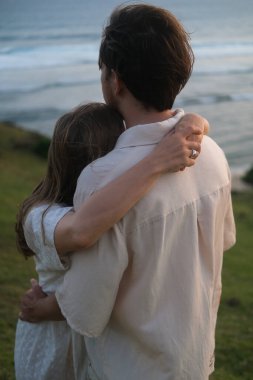 Genç kadın ve erkek doğada gün batımına karşı sarılıyorlar. Balayı gezisi, düğünden sonra aşık bir çift. Tepedeki okyanusta romantik bir randevu. Sevgililer Günü. Aşk ve romantik ilişkiler.