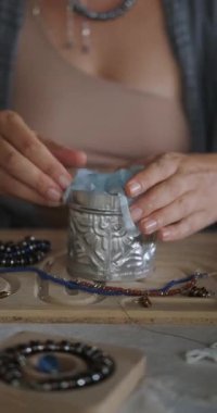 Mücevher tasarımcısı bir kadının ellerine yakın çekim. İş yerinde oturuyor, yarattığı mücevherleri bir kutuya koyup bir müşteriye gönderiyor. Küçük ev işleri. Başla. Paketleme işlemi.
