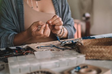 Kadın mücevher tasarımcısı ellerinizi yakın tutun. Üzerinde aletler olan bir çalışma alanında oturuyor ve oltaya boncuk takarak mücevher yapıyor. Mücevher üretme süreci. Küçük işletme. 