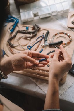 Kadın mücevher tasarımcısı ellerinizi yakın tutun. Üzerinde aletler olan bir çalışma alanında oturuyor ve oltaya boncuk takarak mücevher yapıyor. Mücevher üretme süreci. Küçük işletme. 