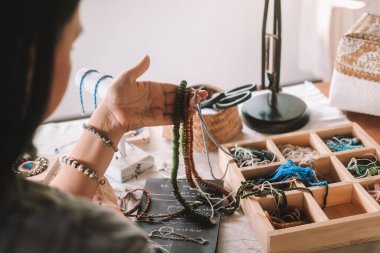 Mücevher tasarımcısı bir kadının ellerine yakın çekim. Masasında oturmuş yarattığı mücevherleri düzenliyor ve bir deftere fikirler yazıyor. Mücevher yapma işlemi. Küçük ev işleri. Açılış.