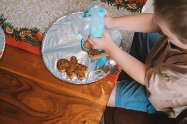 Kardan adam şeklinde zencefilli kurabiyeyi kremayla süsleyen bir çocuk eli. Çocuklar için bir tatil pişirme atölyesi. Yeni Yıl ve Noel için Hazırlık.