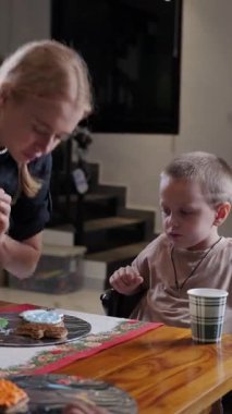 Bir kadın pasta şefi çocuklara Noel kurabiyesini nasıl süslemeleri gerektiğini öğretiyor. Bir pasta poşeti tutuyor ve çocuklara göstererek zencefilli ekmeğin üzerine resim çiziyor. Çocuklar için şenlik atölyesi