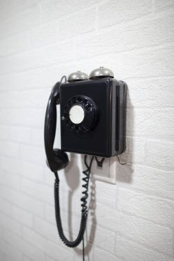 Beyaz bir duvarda eski siyah bir telefon. Teknoloji değişkenliği kavramı.