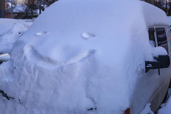 Parked minibus is completely covered in deep snow with a smiley face on it.