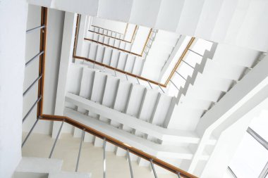 Tahta tırabzanlar ve metal parmaklıklarla beyaz spiral bir merdivene bakarak çizgiler ve açılarla soyut bir geometrik desen yaratıyor..