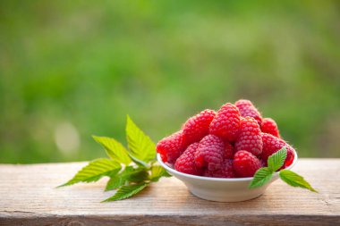 Bir kase ahududu ve yeşil arka planda birkaç yaprak, tatlı yaz meyvesi. Yakın çekim, doğal ışık, boşluğu kopyala.