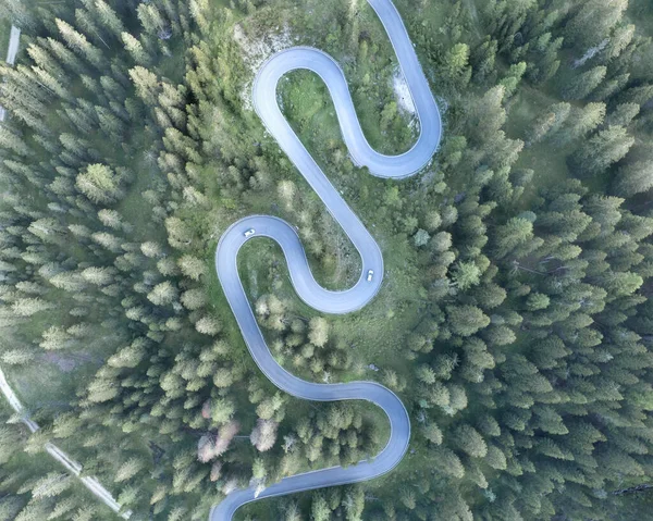 Ormanda atmosferik bir dağ yolu, yılan dönüşleriyle, Dolomitlerin kalbindeki dron tarafından yukarıdan fotoğraflanmış.
