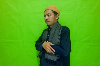 Asian muslim man standing with hand in chest are doing salat isolated on green background clipart
