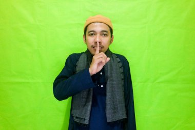 Asyalı Müslüman Adam 'ın sessiz portresi, yeşil arka planda izole edilmiş sessiz bir jest (kapa çeneni) tutun