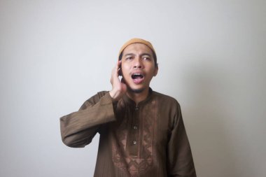 Dindar Müslüman adam, beyaz arka planda izole edilmiş Azan ya da İqamah 'ı okuyor.