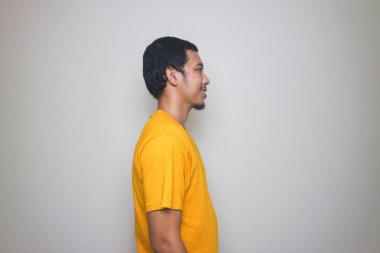 Beyaz arka planda izole edilmiş sarı tişörtle gülümseyen Asyalı adam.