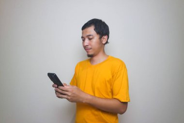 Resmi tişörtlü yakışıklı Asyalı genç adam akıllı telefon ticareti yapıyor ya da kahverengi izole stüdyo arka planında sohbet ediyor..