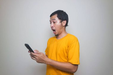 Resmi tişörtlü yakışıklı Asyalı genç adam akıllı telefon ticareti yapıyor ya da kahverengi izole stüdyo arka planında sohbet ediyor..