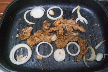 Mutfakta cımbızla leziz et yüzeyini gösterirken, fırında ince et dilimleri kızartan tanınmamış bir aşçı.