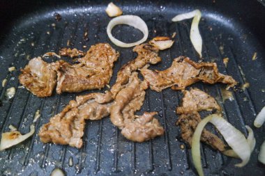 Mutfakta cımbızla leziz et yüzeyini gösterirken, fırında ince et dilimleri kızartan tanınmamış bir aşçı.