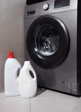 Zeminde deterjan şişeleri olan ön yükleme makinesi. Ev temizliği kavramı, modern çamaşır odası, deterjan reklamı veya akıllı ev teknolojisi..