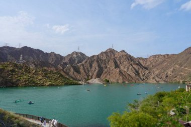 Ön planda turkuaz yeşil su, arka planda dramatik dağlar ve yukarıda yumuşak bir gökyüzü bulunan çarpıcı bir doğal manzara.. 