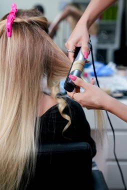 Kuaför, kuaförde düz ütülü sarı saç kıvırıyor. Saç şekillendirme sürecinde yarı düz ve yarı kıvırcık saçlı bir kadının arka görünüşü. Görünür kıllı eller
