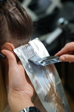 Saç aydınlatma işlemine yakın çekim. Saç telleri, mavi beyazlatma tozu sürülmüş ve güzellik salonundaki sarışın dönüşümüne hazırlanıyor.