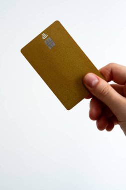 Sarı bir banka kartını beyaz arka planlı basit bir kompozisyonda tutan kişi, modern finans ve nakit işlemlerini sembolize ediyor.. 