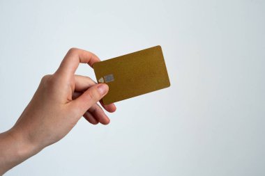 Beyaz arka planda altın bir kredi kartı sunan bir elin yakın çekimi, prim bankacılık, zenginlik ve özel üyeliği sembolize ediyor. 