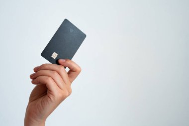 Temiz beyaz arka planda izole edilmiş, çipli, modern siyah bir kredi kartını tutan bir elin yakın çekimi. Finans, bankacılık veya alışveriş kavramları için ideal.