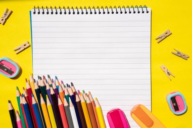 Sarı zemin üzerinde kurşun kalemler ve okul gereçleri olan açık sarmal defter manzarası. Okula geri dön. Fotokopi alanı olan yaratıcı daire.. 