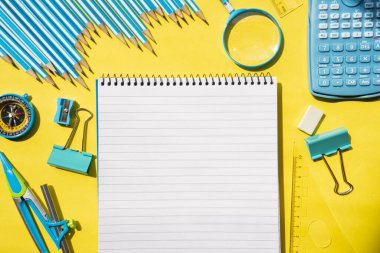 Sarı yüzeydeki sarmal not defteri ve çeşitli kırtasiye malzemeleri. Öğrenim, öğrenim, yaratıcı çalışma alanı ve okul eğitimi kavramı. 