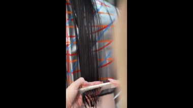 Profesyonel kuaför, kırık uçlarını kesmeden önce koyu renk saç tellerini dikkatlice tarıyor. Güzellik salonu servisi, saç bakımı ve yüksek kaliteli yakın çekim..