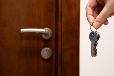 Ahşap bir kapının yanında anahtarı tutan bir el resmi. Taşınmak, mülk kiralamak, gayrimenkul, ev güvenliği ve konut. 