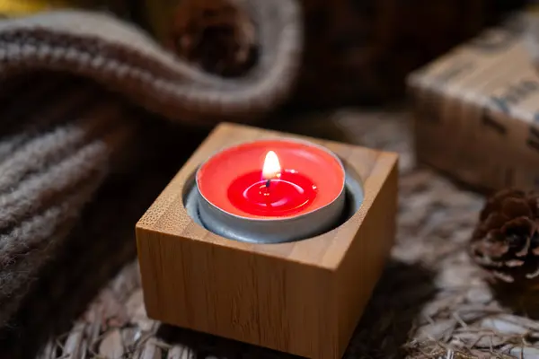 Yumuşak örülmüş bir yüzey ve sıcak bokeh ışıkları üzerinde, kare bir ahşap tutacağında kırmızı bir mumun olduğu minimal bir sahne.. 