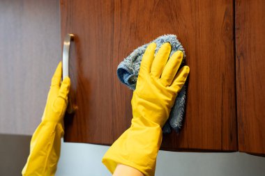 Womans hand in yellow gloves cleaning wooden cabinet door with cloth. Domestic hygiene and household maintenance. 