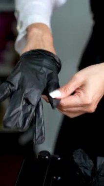 Close-up of female hands with manicure putting on black gloves before salon work. Concept of hygiene, beauty care, safety, and professional service. 