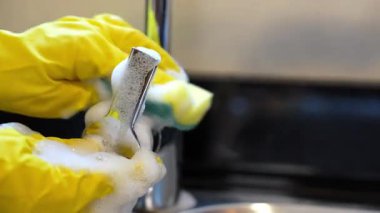 Extreme close-up of hands in yellow gloves cleaning a metal faucet handle with foamy sponge. Perfect for home cleaning, hygiene, and professional cleaning service content. 