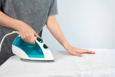 Close-up of female hand using modern iron on fabric, concept of home care, laundry, cleaning, and household chores. 